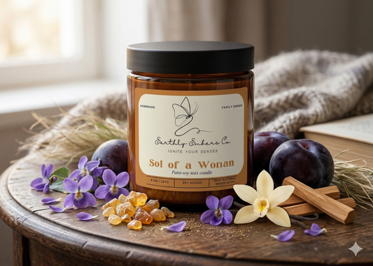 Sol of a Woman 8oz amber jar candle with a black lid and wood wick by Earthly Embers Co. Surrounded by velvet plums, sugared violets, vanilla orchids, and sandalwood on a rustic table, reflecting the luxury fragrance notes of the Velvet Radiance.